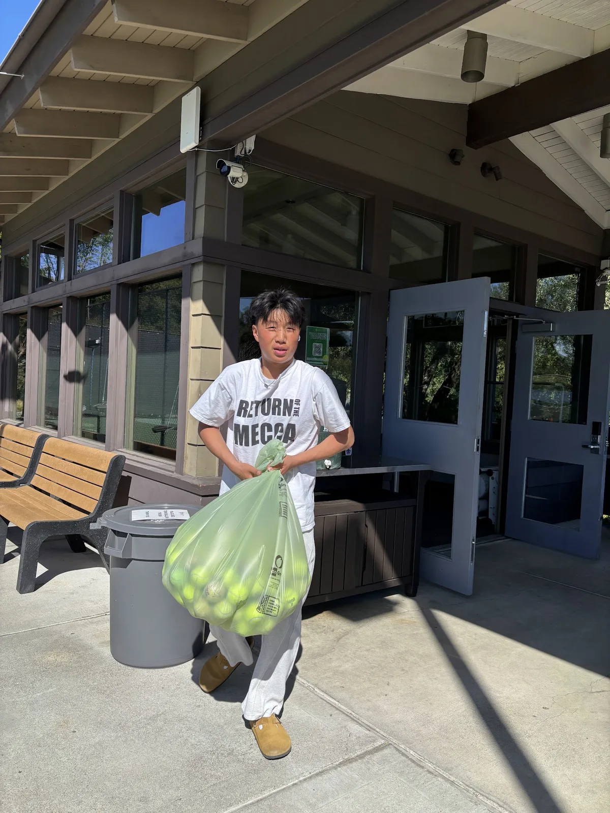 A volunteer carrying a full bag of collected tennis balls out of a club clubhouse