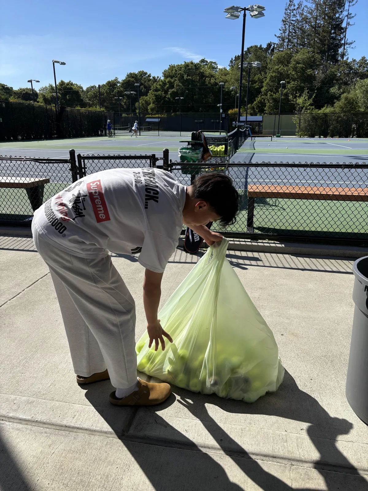 A volunteer tying off a bag of used tennis balls collected courtside at a tennis club