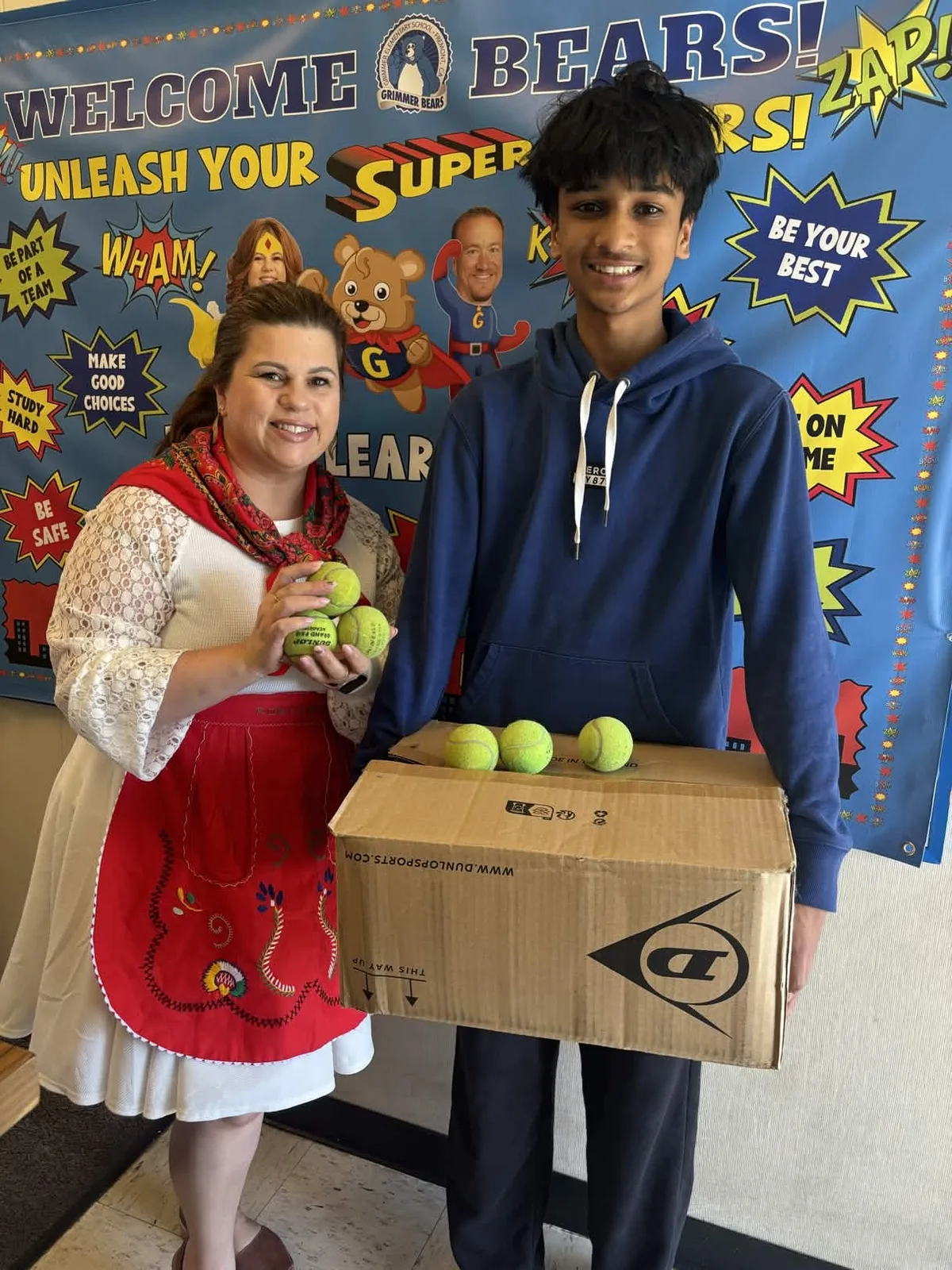A volunteer handing a box of tennis balls to a teacher at an elementary school